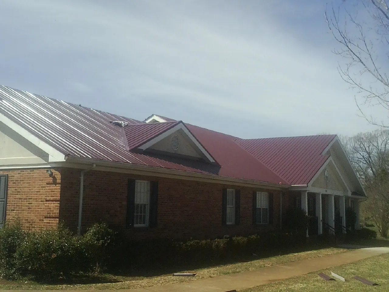 Red metal roof with gabled entries on a long brick building, from a Hail Damage Roof Repair job in Palmyra